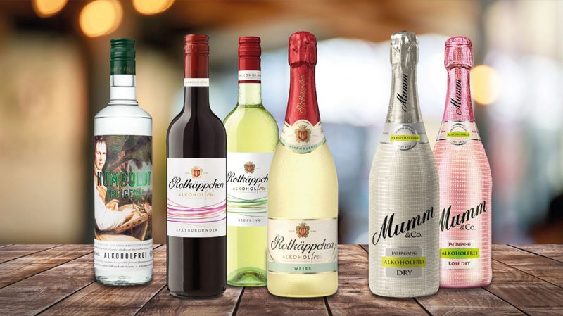 Sechs Flaschen alkoholfreier Getränke stehen auf einem Holztisch, darunter verschiedene Sorten von Rotkäppchen und Mumm.