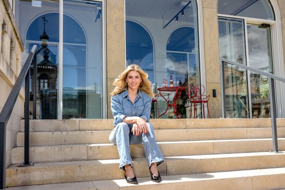 Porträtfoto Silvia Wiesner: In Jeans und schwarzen Schuhen sitzt sie auf den Stufen vor dem Pavillon der Rotkäppchen Erlebniswelt