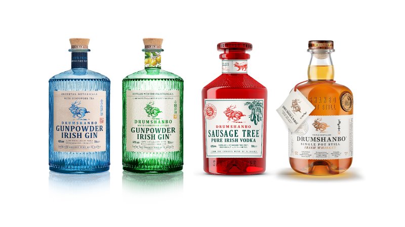 Vier Flaschen von Drumshanbo Spirituosen stehen nebeneinander, jede mit einzigartigem Design und Farbe, auf einem reflektierenden Untergrund.