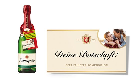 Eine Flasche Rotkäppchen Sekt steht neben einer eleganten Karte mit der Aufschrift 'Deine Botschaft!' und einem glücklichen Paar.