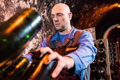 In a cool cellar environment, a man tends to bottles, his hands precise and purposeful at work.