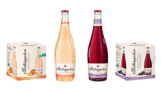 Zwei Flaschen Rotkäppchen Fruchtsecco stehen zwischen zwei Verpackungen, eine mit Pfirsichgeschmack und die andere mit schwarzer Johannisbeere.