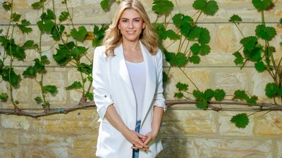 Porträtfoto Silvia Wiesner: Sie trägt einen weißen Blazer und Jeans, während sie entspannt mit gefalteten Händen vor einer natürlichen Kulisse posiert.