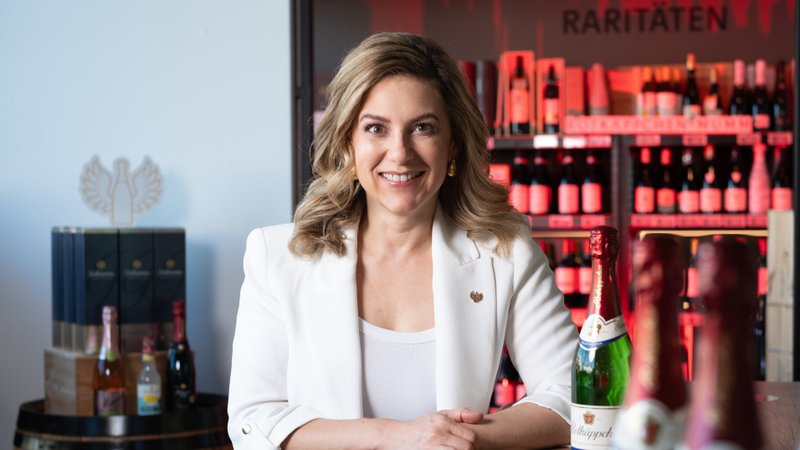 Silvia Wiesner an einem Holztisch mit Sektflaschen, im Hintergrund Weinregale mit Raritäten.