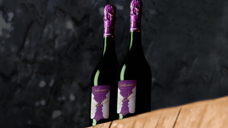 Zwei Flaschen Sekt stehen auf einem Holzbrett, mit eleganten lila Kappen und einem stilvollen Etikett im Hintergrund.