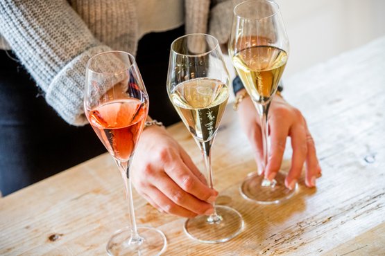 Drei elegante Sektgläser stehen auf einem Holztisch, während eine Hand das Glas mit dem rosafarbenen Getränk hält.