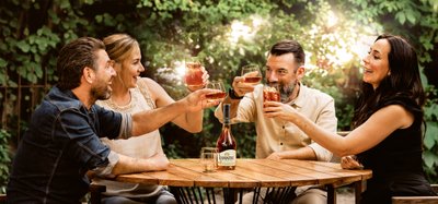 Vier Freunde stoßen fröhlich mit Getränken an einem Holztisch in einem grünen Garten an, umgeben von einer entspannten Atmosphäre.