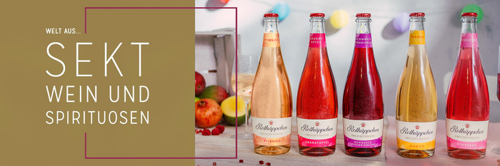 Fünf Flaschen Fruchtsecco in verschiedenen Geschmacksrichtungen stehen auf einem Tisch, umgeben von bunten Dekorationen.