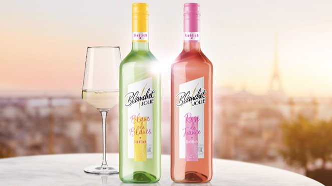 Zwei Flaschen Wein Blanchet stehen auf einem Tisch, eine grüne und eine rosafarbene, mit einem Glas Weißwein daneben.