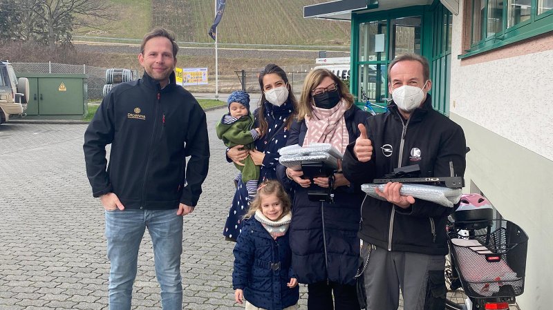 Eine Gruppe von fünf Personen steht lächelnd vor einem Gebäude, während sie verschiedene Gegenstände in den Händen halten.