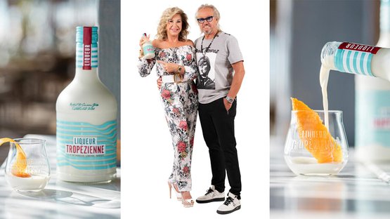 Das Paar strahlt Freude aus, während sie den Liqueur Tropezienne präsentieren, der in einem eleganten Glas serviert wird.