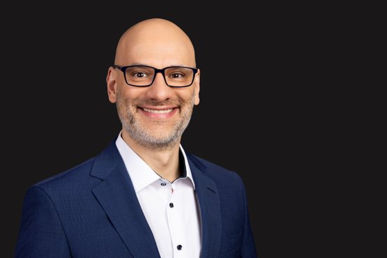 Markus Jauch: The man with a friendly smile has a grey beard and wears glasses while looking into the camera.