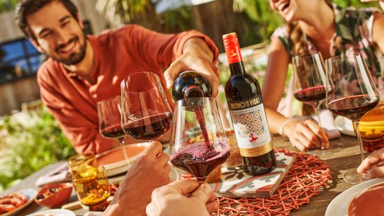 Ein fröhliches Zusammensein im Freien, wo Wein eingeschenkt wird und die Freunde mit Lachen und Freude den Moment genießen.