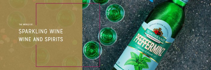 A bottle of peppermint liqueur lies on a gray background, surrounded by green glasses.