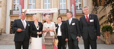 A group of six people pose in front of a festive backdrop decorated with banners and decorations.