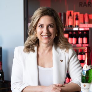 Silvia Wiesner an einem Holztisch mit Sektflaschen, im Hintergrund Weinregale mit Raritäten.